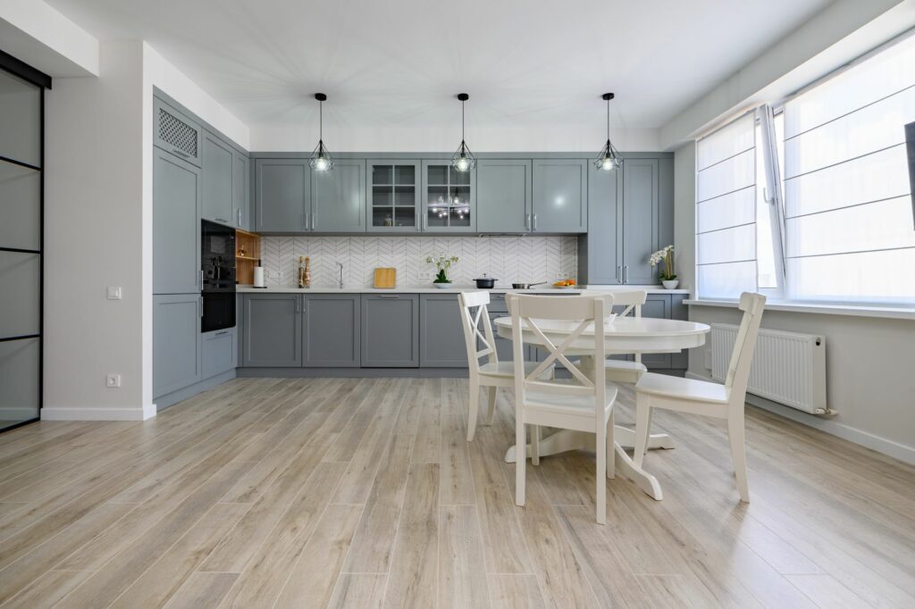 gray shaker kitchen cabinets with wood look flooring white dining set subway tile backsplash and bright natural light kitchen design