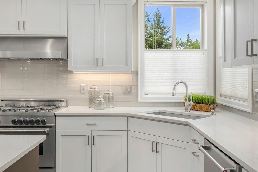 white kitchen cabinets with quartz countertops stainless steel appliances and bright natural light
